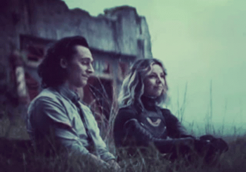A Man And A Woman Are Sitting In The Grass Looking At Something . GIF