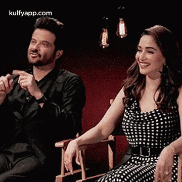 A Man And A Woman Are Sitting Next To Each Other And Smiling . GIF