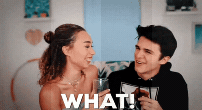 A Man And A Woman Are Sitting Next To Each Other And The Woman Is Holding A Glass That Says What ! GIF