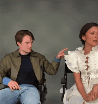 A Man And A Woman Are Sitting Next To Each Other And The Woman Is Pointing At The Man GIF