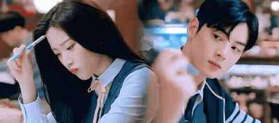 A Man And A Woman Are Sitting Next To Each Other In A Restaurant . The Woman Is Holding A Pen In Her Hand . GIF