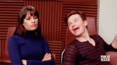 A Man And A Woman Are Sitting Next To Each Other In A Room . The Man Is Making A Funny Face . GIF