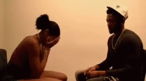 A Man And A Woman Are Sitting Next To Each Other In A Room . The Woman Is Covering Her Face With Her Hands . GIF