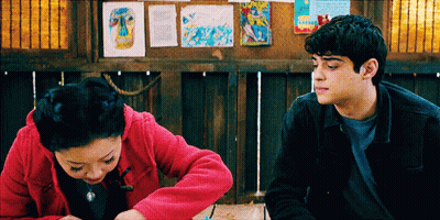 A Man And A Woman Are Sitting Next To Each Other In Front Of A Bulletin Board GIF