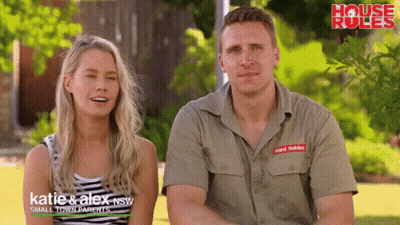 A Man And A Woman Are Sitting Next To Each Other In Front Of A Sign That Says " House Rules " GIF