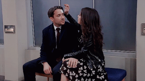 A Man And A Woman Are Sitting Next To Each Other On A Bench . The Woman Is Touching The Man 'S Face . GIF
