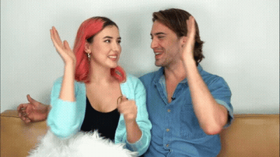 A Man And A Woman Are Sitting Next To Each Other On A Couch And The Woman Has Pink Hair GIF