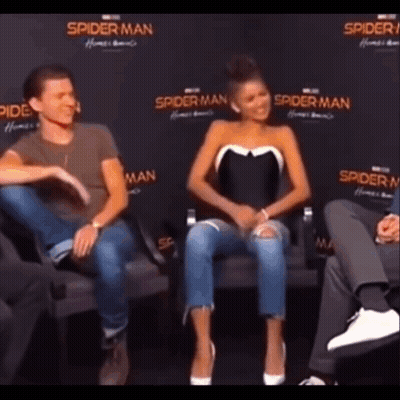A Man And A Woman Are Sitting Next To Each Other On A Couch In Front Of A Spider Man Sign . GIF