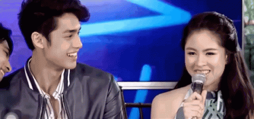 A Man And A Woman Are Sitting Next To Each Other With A Microphone . GIF