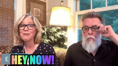 A Man And A Woman Are Sitting Next To Each Other With The Words Hey Now Behind Them GIF