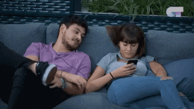A Man And A Woman Are Sitting On A Couch And Looking At Their Phones . GIF