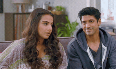 A Man And A Woman Are Sitting On A Couch And Smiling At Each Other GIF