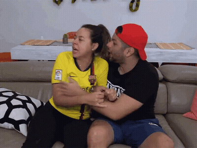 A Man And A Woman Are Sitting On A Couch And The Woman Is Wearing A Yellow Shirt That Says Barça GIF