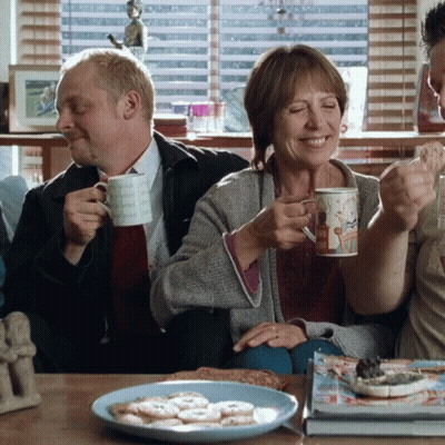 A Man And A Woman Are Sitting On A Couch Drinking Coffee And Smiling GIF