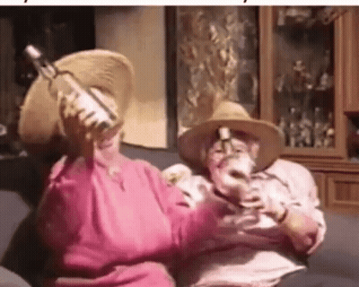 A Man And A Woman Are Sitting On A Couch Drinking Wine And Holding Bottles . GIF