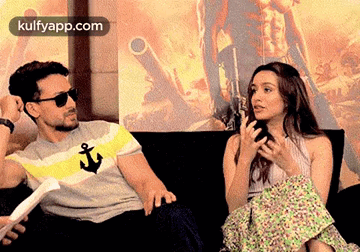 A Man And A Woman Are Sitting On A Couch Talking . GIF