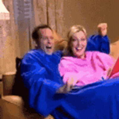 A Man And A Woman Are Sitting On A Couch Wearing Blankets GIF
