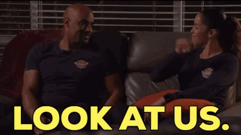 A Man And A Woman Are Sitting On A Couch With The Words " Look At Us " Behind Them GIF