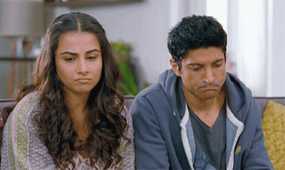 A Man And A Woman Are Sitting On A Couch With Their Faces Turned Towards The Camera GIF