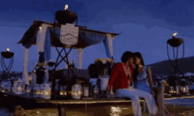 A Man And A Woman Are Sitting On A Dock Kissing Each Other GIF