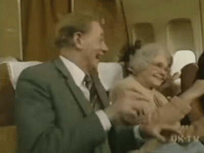 A Man And A Woman Are Sitting On A Plane Laughing And Hugging Each Other . GIF