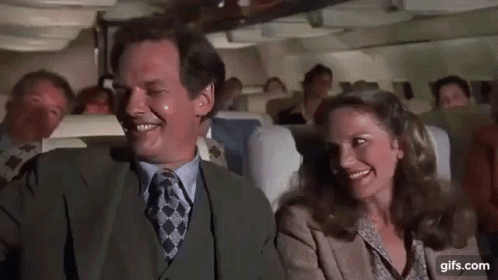 A Man And A Woman Are Sitting On A Plane Laughing And Smiling . GIF
