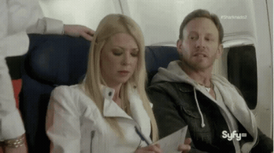 A Man And A Woman Are Sitting On A Plane . The Woman Is Writing On A Piece Of Paper . GIF