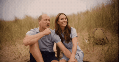 A Man And A Woman Are Sitting On A Sandy Field GIF