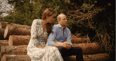 A Man And A Woman Are Sitting On Logs Holding Hands GIF