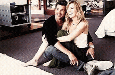 A Man And A Woman Are Sitting On The Floor Hugging Each Other And Smiling . GIF