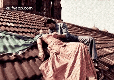 A Man And A Woman Are Sitting On Top Of A Roof . GIF