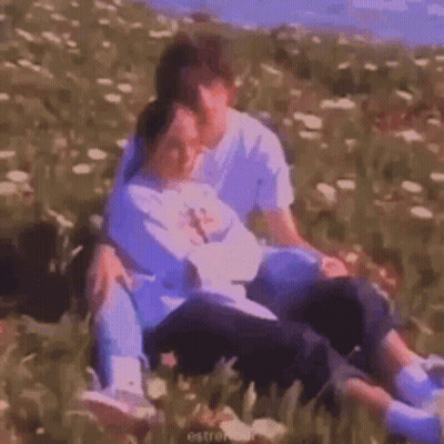 A Man And A Woman Are Sitting On Top Of Each Other In A Field Of Flowers . GIF