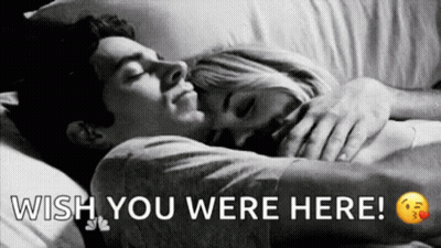A Man And A Woman Are Sleeping In A Bed With The Words `` Wish You Were Here '' Written Above Them . GIF