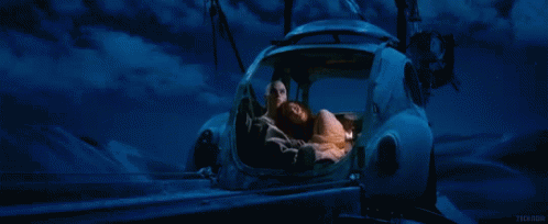 A Man And A Woman Are Sleeping In A Car With A Blue Sky Behind Them GIF
