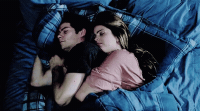 A Man And A Woman Are Sleeping Next To Each Other In A Bed . GIF
