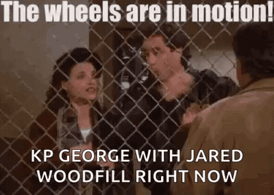 A Man And A Woman Are Standing Behind A Chain Link Fence . GIF
