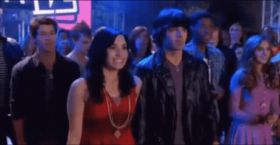 A Man And A Woman Are Standing In A Crowd Of People At A Party . GIF