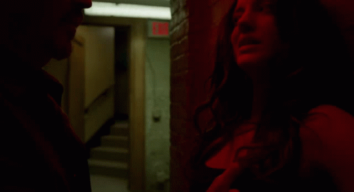 A Man And A Woman Are Standing In A Dark Room With A Red Exit Sign In The Background GIF