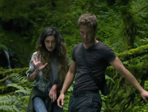 A Man And A Woman Are Standing In A Forest GIF
