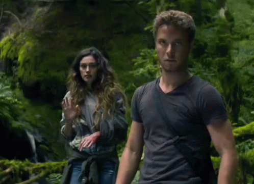 A Man And A Woman Are Standing In A Forest GIF