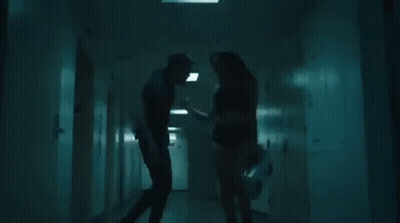 A Man And A Woman Are Standing In A Hallway . GIF