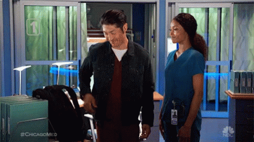 A Man And A Woman Are Standing In A Hospital Hallway . GIF