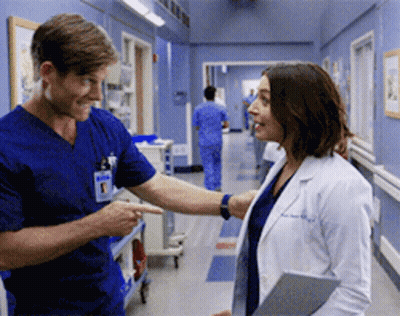 A Man And A Woman Are Standing In A Hospital Hallway GIF