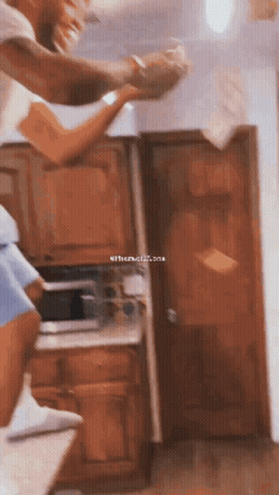 A Man And A Woman Are Standing In A Kitchen Holding Hands While The Woman Throws Papers In The Air . GIF
