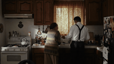A Man And A Woman Are Standing In A Kitchen GIF