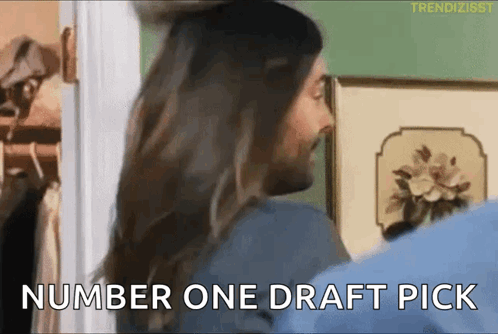 A Man And A Woman Are Standing In A Room And The Man Is Saying Number One Draft Pick GIF