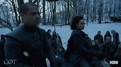 A Man And A Woman Are Standing In A Snowy Forest With The Word Got On The Bottom GIF