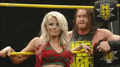 A Man And A Woman Are Standing In A Wrestling Ring Holding Yellow Ropes . GIF