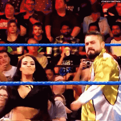 A Man And A Woman Are Standing In A Wrestling Ring With A Crowd Watching . GIF