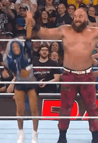 A Man And A Woman Are Standing In A Wrestling Ring With Their Arms In The Air . GIF